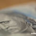 Detalhe ampliado de uma nota de real, destacando o rosto em foco suave, simbolizando dinheiro, pagamento e recebimento de valores, com logo do LCbank.